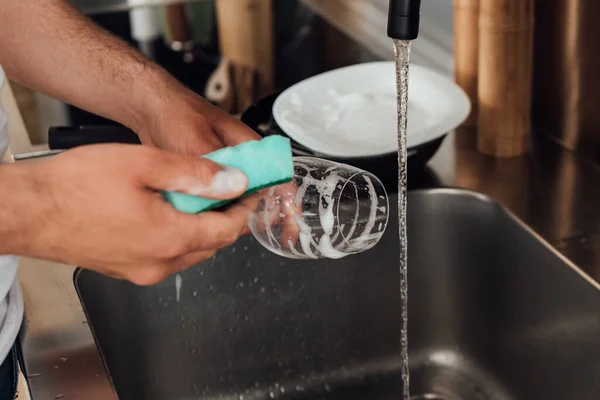 Vista cortada do homem limpando copo de vinho com esponja na cozinha — Fotografia de Stock