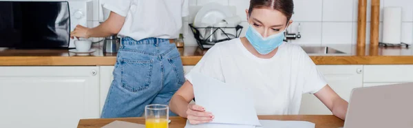 Concetto panoramico di donna in maschera medica guardando carta bianca vicino sorella — Foto stock