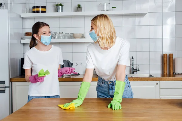 Сестры в медицинских масках и латексных перчатках держат тряпки во время работы по дому — стоковое фото