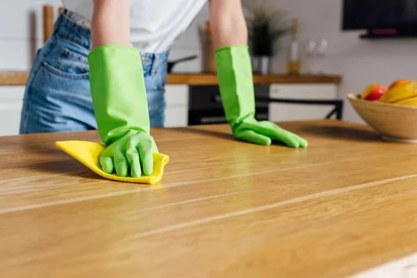 Ausgeschnittene Ansicht einer Frau in Gummihandschuhen, die Lappen am Tisch hält — Stockfoto