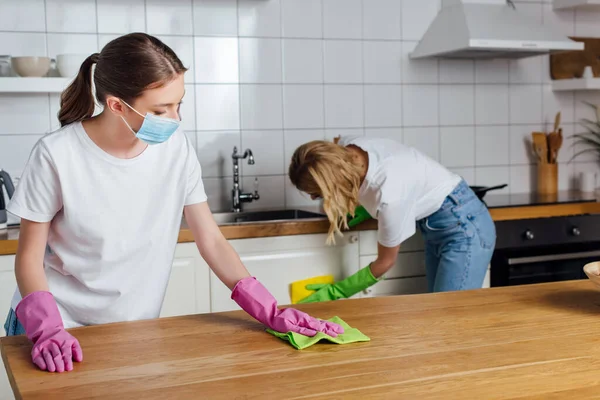 Enfoque selectivo de chica en máscara médica y hermana haciendo tareas domésticas cocina - foto de stock