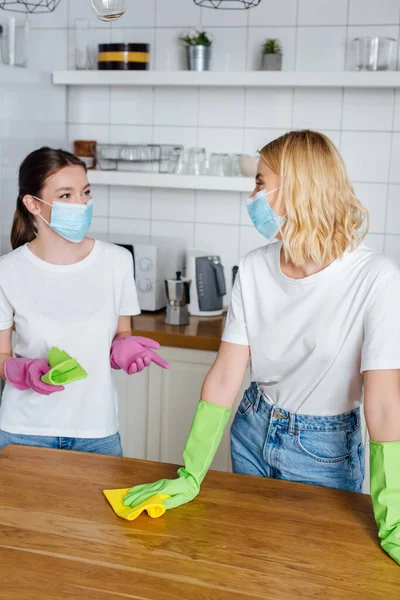 Sisters in medical masks and latex gloves holding rags while looking at each other — Stock Photo