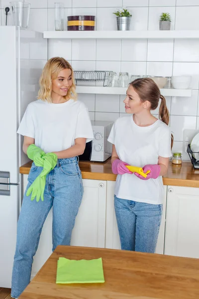 Enfoque selectivo de hermanas alegres en guantes de goma mirándose entre sí - foto de stock