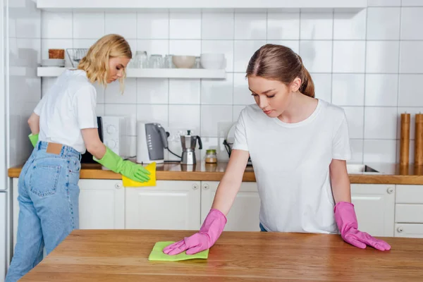 Messa a fuoco selettiva delle sorelle in guanti di gomma che tengono stracci durante la pulizia della cucina — Foto stock
