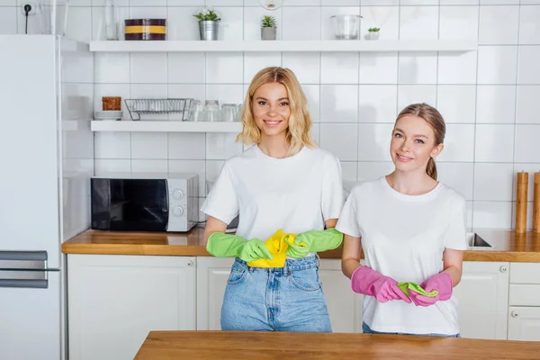 Fröhliche Schwestern in Gummihandschuhen, die in der Küche in die Kamera schauen — Stockfoto