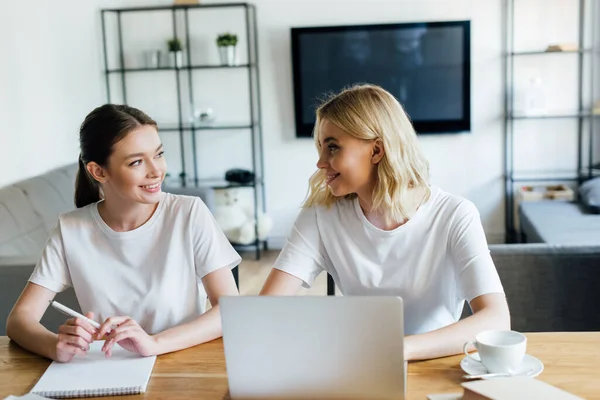 Happy sisters looking at each other near laptop and notebook — Stock Photo