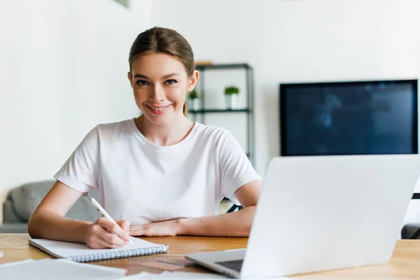 Fuoco selettivo della donna felice che tiene la penna vicino al notebook e al computer portatile — Foto stock