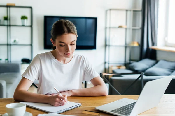 Селективный фокус красивой женщины, пишущей в ноутбуке рядом с ноутбуком и чашкой кофе, концепция онлайн исследования — стоковое фото