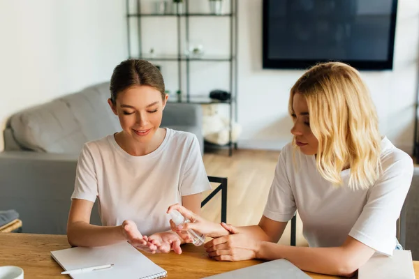 Woman holding bottle with hand sanitizer near cheerful sister at home — Stock Photo