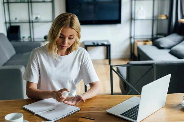 Schöne Frau mit Flasche mit Händedesinfektionsmittel in der Nähe von Laptop und Kreditkarte auf dem Tisch — Stockfoto