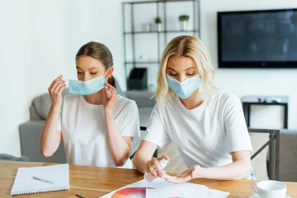 Mulher usando máscara médica perto da irmã segurando higienizador de mão em casa — Fotografia de Stock