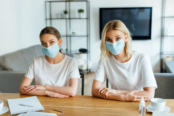 Sisters in medical masks near credit card and cups on table — Stock Photo
