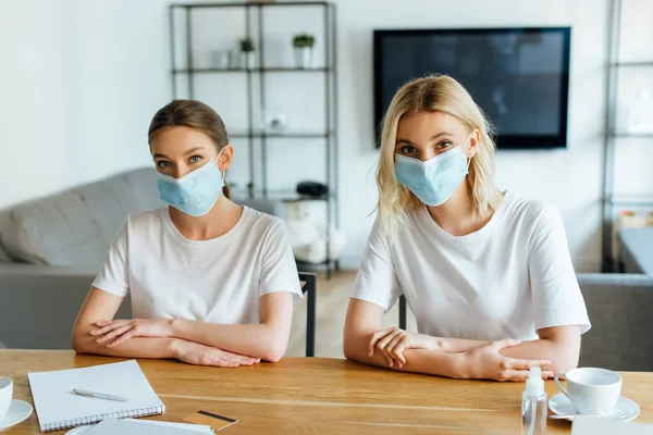 Irmãs em máscaras médicas perto de cartão de crédito e copos na mesa — Fotografia de Stock