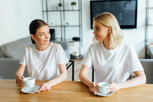 Attractive sisters looking at each other while holding cups of coffee — Stock Photo