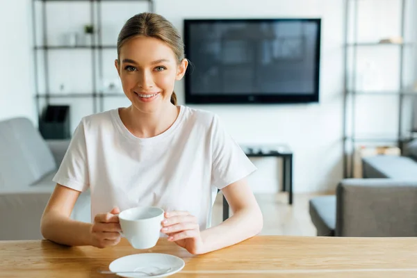 Mujer alegre mirando a la cámara y sosteniendo la taza de café - foto de stock