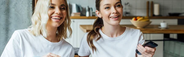 Panoramic shot of cheerful sisters watching movie at home — Stock Photo