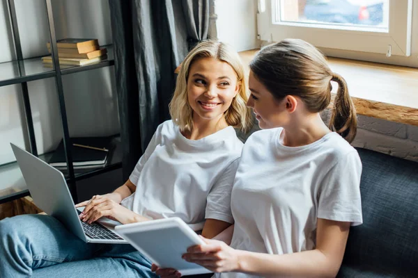 Selektiver Fokus von Schwestern, die einander anlächeln, während sie zu Hause digitales Tablet und Laptop benutzen — Stockfoto