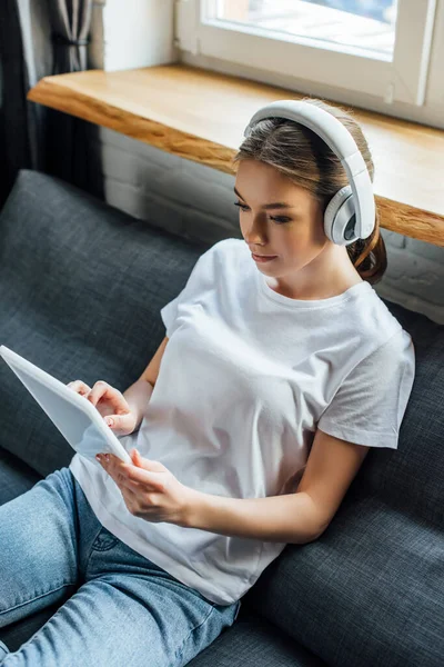 Menina atraente em fones de ouvido usando tablet digital na sala de estar — Fotografia de Stock