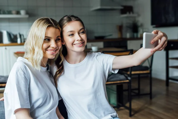 Красиві усміхнені сестри беруть селфі зі смартфоном вдома — стокове фото
