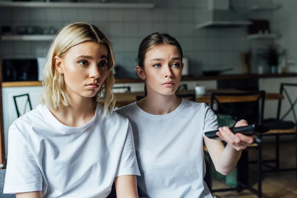 Sad girl sitting near sister while watching tv at home — Stock Photo