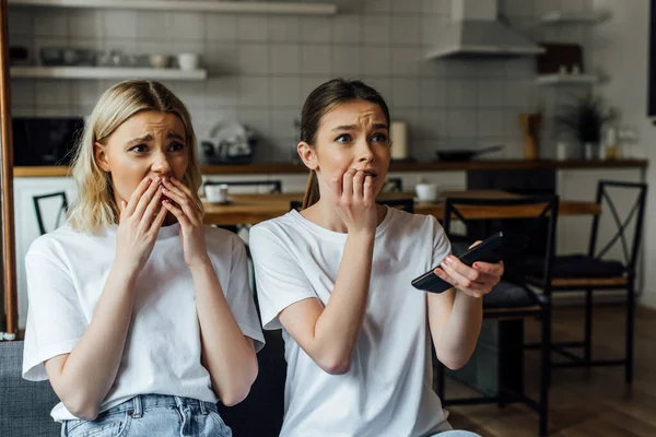 Shocked and scared sisters watching tv on couch at home — Stock Photo