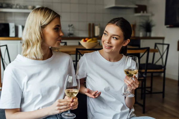 Hermanas sonrientes hablando mientras sostienen vasos de vino en casa - foto de stock