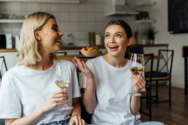Hermanas alegres hablando mientras sostienen copas de vino en casa - foto de stock