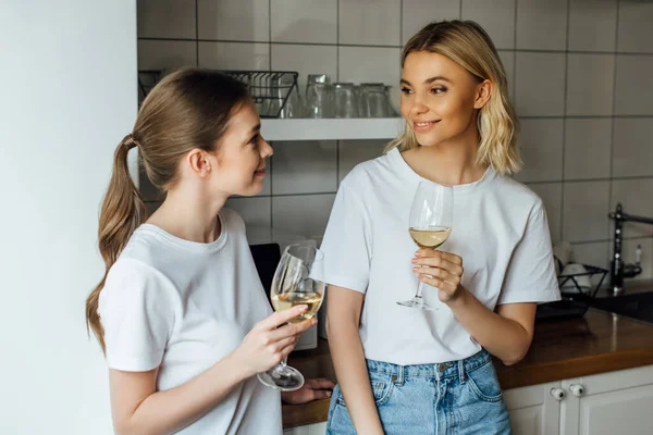 Smiling sisters holding glasses of wine in kitchen — Stock Photo