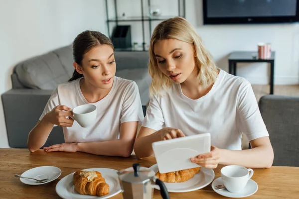 Enfoque selectivo de hermanas usando tableta digital durante el desayuno en la cocina - foto de stock