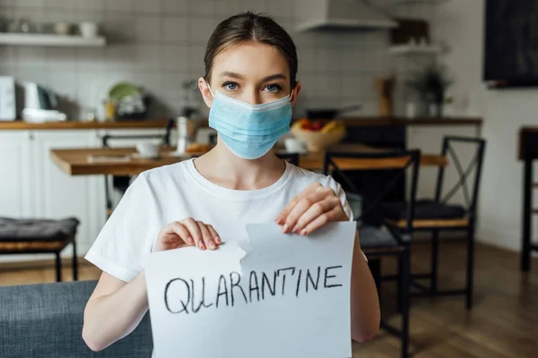 Girl in medical mask tearing card with quarantine lettering at home — Stock Photo
