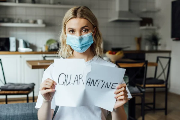 Woman in medical mask tearing card with quarantine lettering at home — Stock Photo