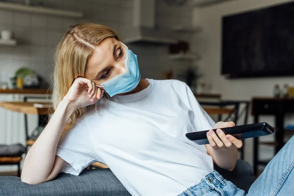 Ragazza bionda in maschera medica guardando film in soggiorno — Foto stock