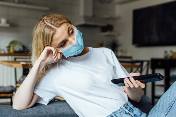 Chica rubia en máscara médica viendo la película en la sala de estar - foto de stock