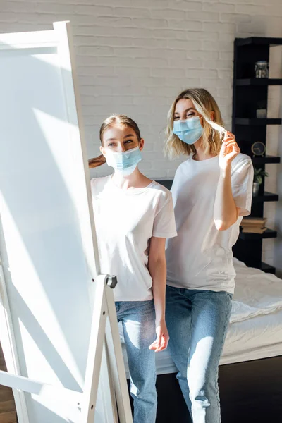 Младшие сестры в медицинских масках смотрят в зеркало в спальне — стоковое фото