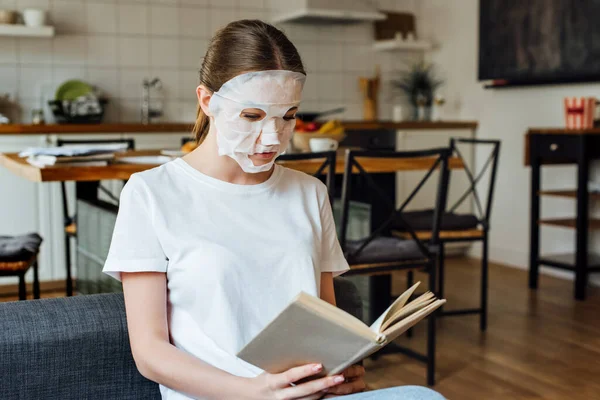 Selective focus of young woman in face mask reading book at home — Stock Photo