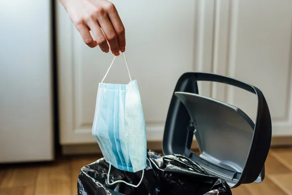 Vista recortada de la mujer sosteniendo máscara médica cerca de bote de basura - foto de stock