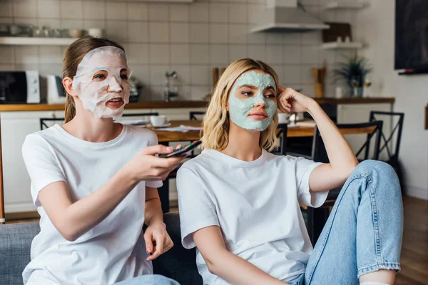 Sisters in face masks watching tv on couch at home — Stock Photo