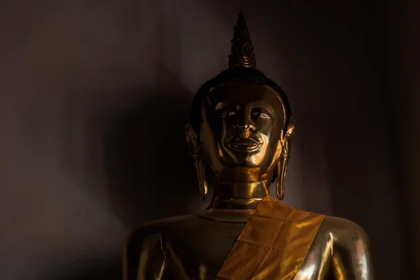 Eine Statue des Goldbuddhas mit Schatten an der Wand im dunklen Raum. — Stockfoto
