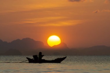 Gün batımında büyük güneş gölde gökyüzünde siluet dağı ve balıkçı teknesiyle