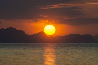 Gün batımında güneş, gölün göbeğinde, siluet dağında.