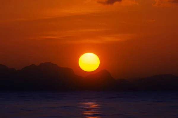 Big sun on sunset sky at the lake with silhouette mountain