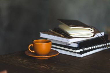 Close-up view of cup of coffee and notebooks on wooden table top clipart