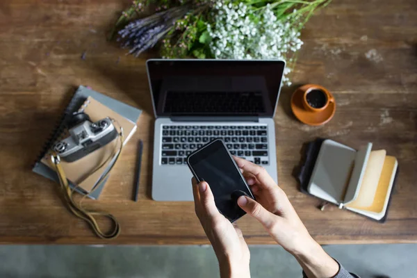 Человек, использующий смартфон и ноутбук на рабочем месте с ноутбуками и винтажной камерой — стоковое фото