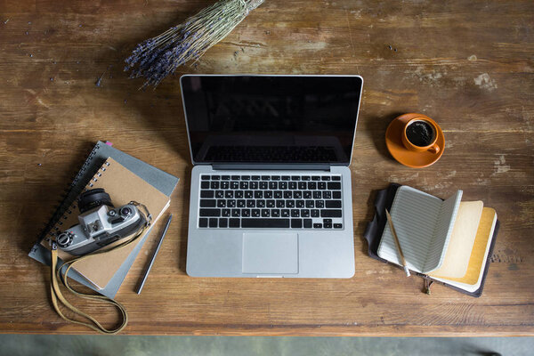 top view of laptop, diaries, vintage photo camera and cup of coffee on wooden tabletop