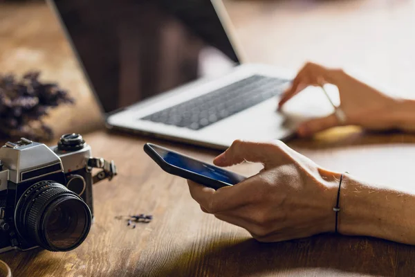 Personne utilisant un ordinateur portable et smartphone à l'espace de travail avec un appareil photo vintage — Photo