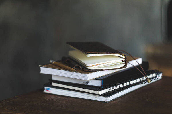 Close-up view of stacked notebooks and pencil on dark table 