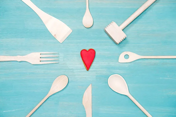 Vista dall'alto di vari utensili da cucina in legno con simbolo del cuore sul tavolo blu — Foto Stock