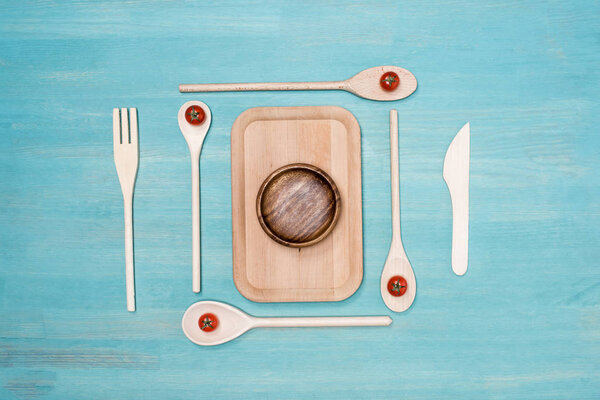 Top view of wooden cutting board with kitchen utensils and cherry tomatoes on table