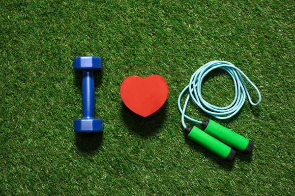 Top view of colorful dumbbell with heart symbol and skipping rope on the grass — Stock Photo, Image