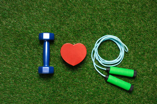 colorful dumbbell with heart symbol and skipping rope on the grass